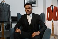 A stylish man in a tailored suit seated inside a fashion showroom, exuding elegance.